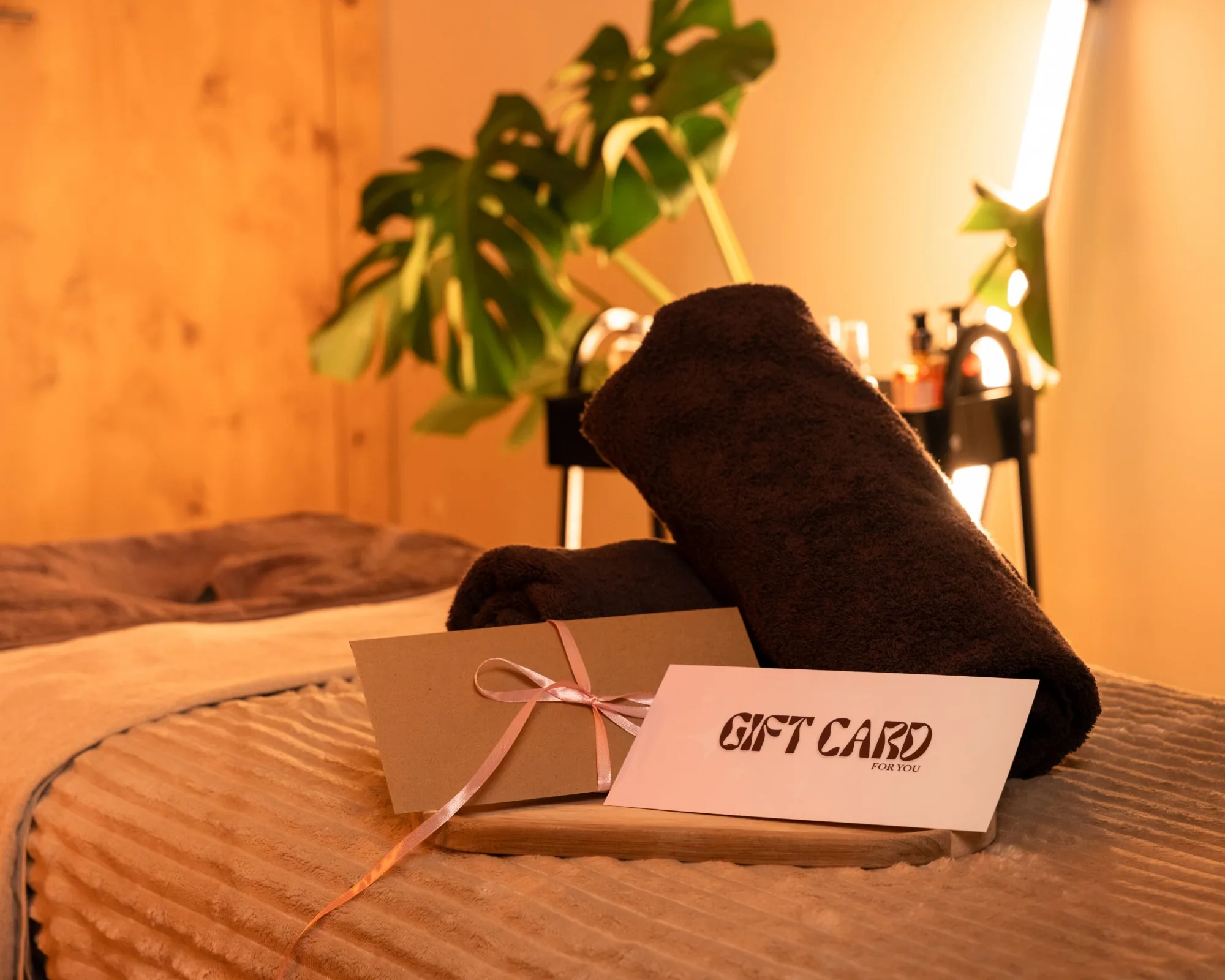 Gift card na masaż w kopercie z różową wstążką w gabinecie z monsterą, ujęcie poziome